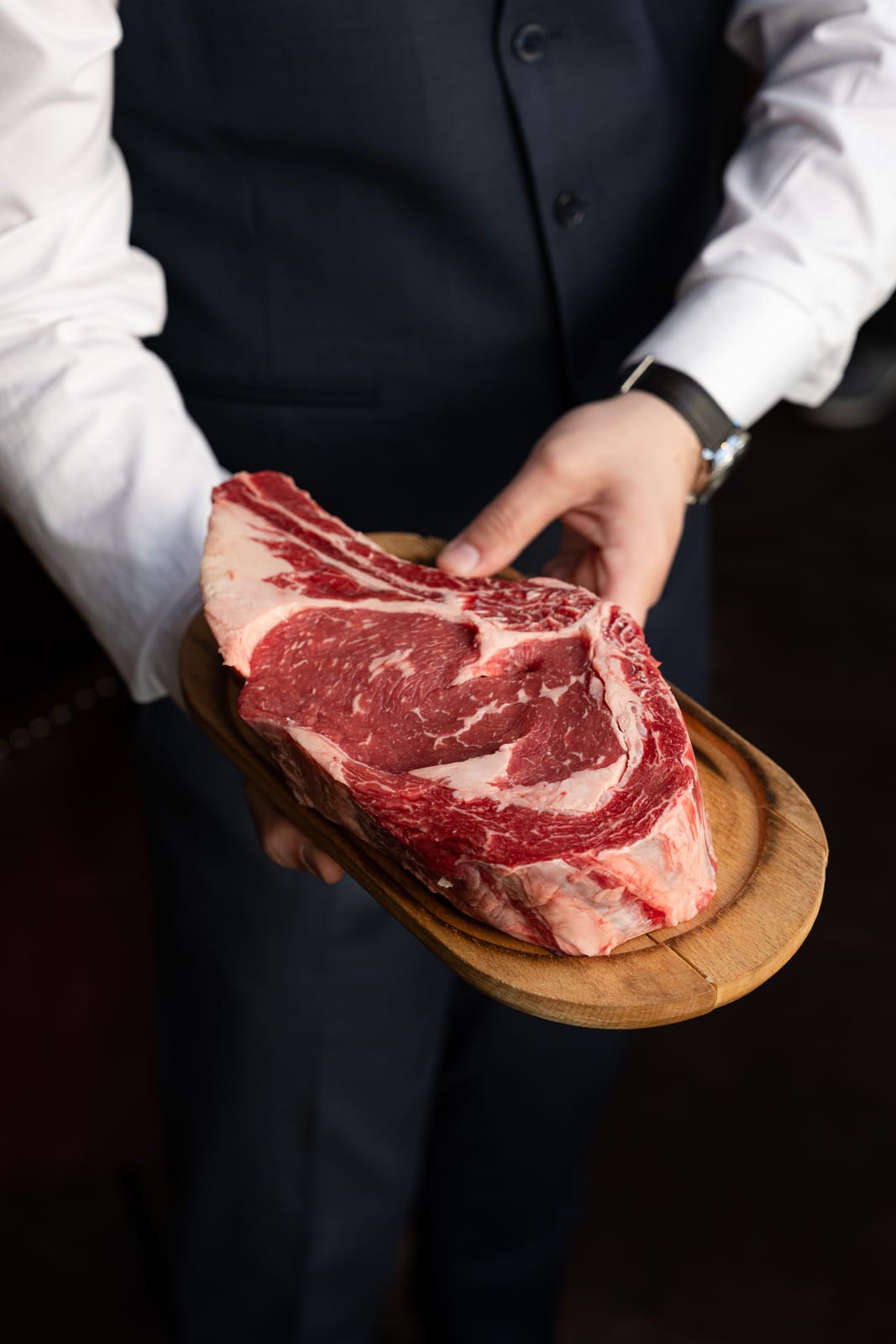 Un membre de l'équipe en gilet présente une côte de bœuf crue posée sur une planche en bois
