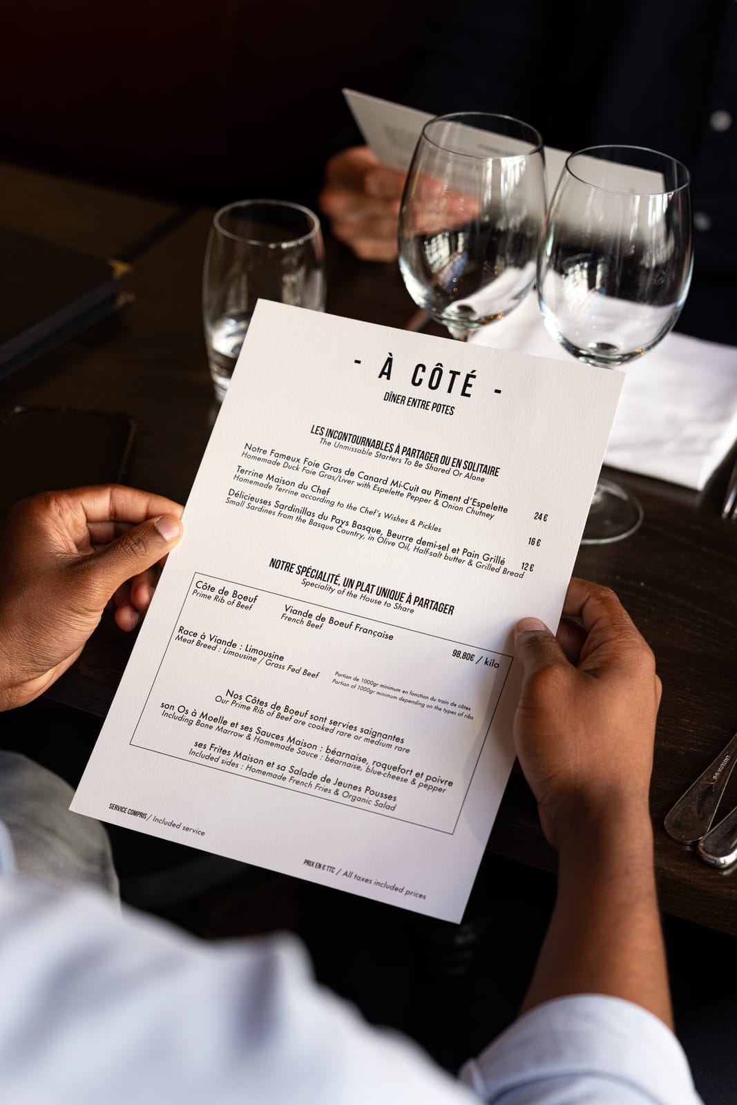 Un convive consulte la carte d'À Côté, présentant la côte de bœuf française de race limousine à partager