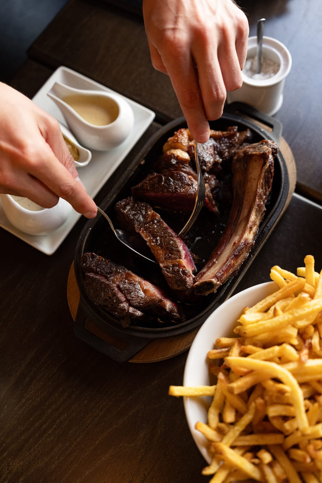 Côte de bœuf découpée servie dans un poêlon en fonte avec frites et sauces maison